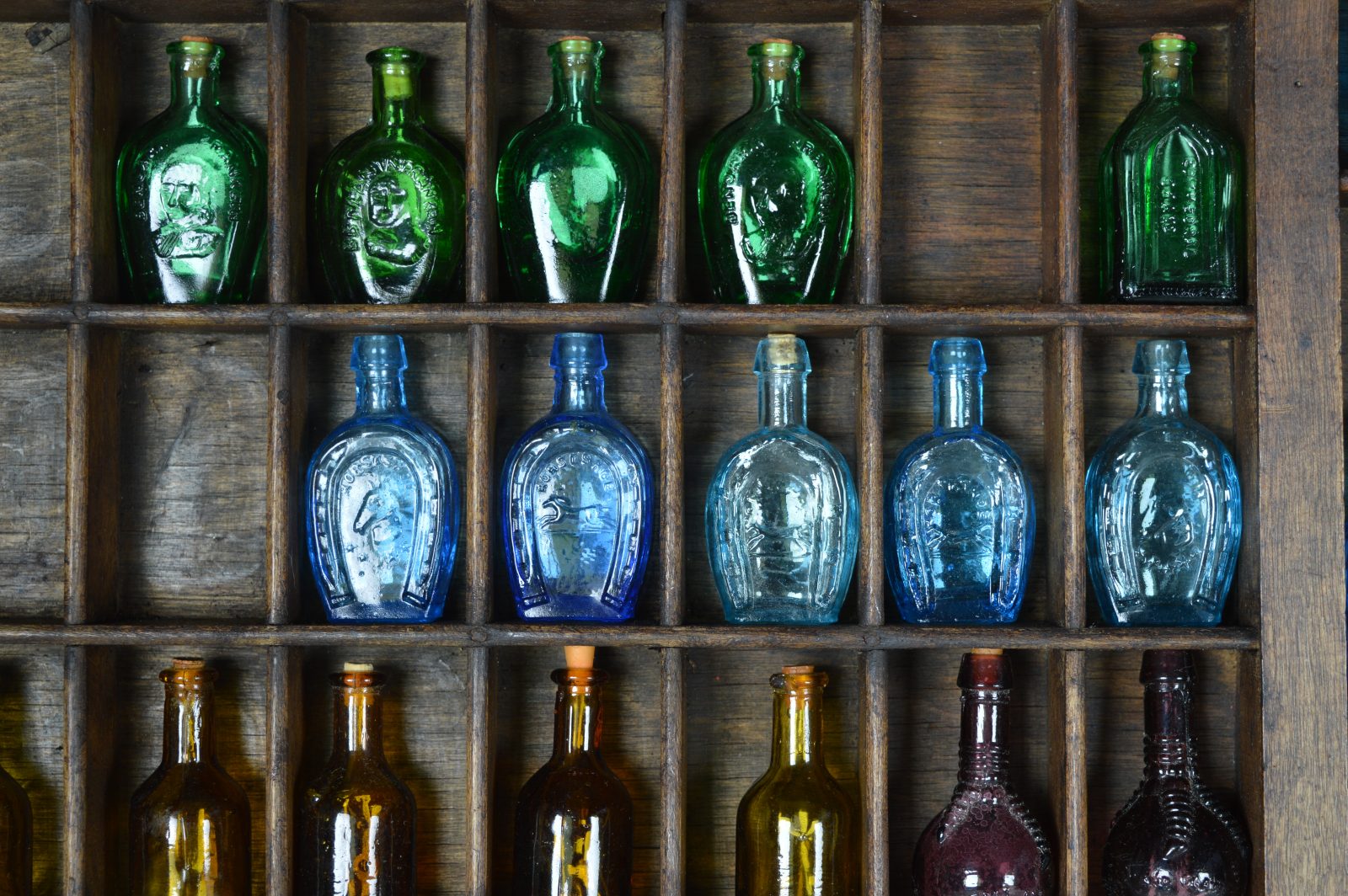 Letterbak met gekleurde glazen flesjes in blauw, groen, bruin en paars